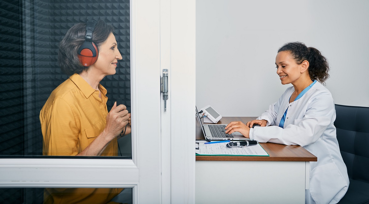 Audiologist giving patient a hearing test in a hearing booth