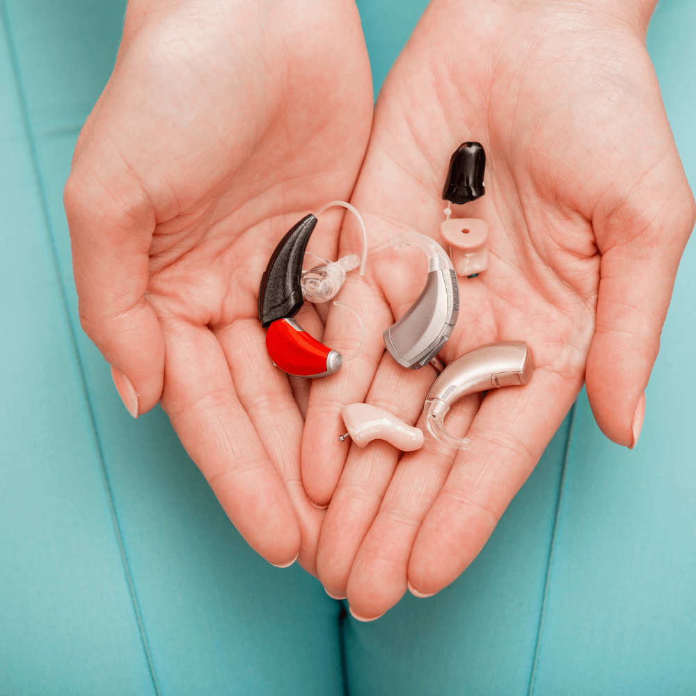 Two hands holding assortment of hearing aids